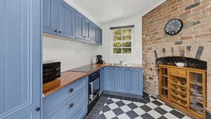 Een keuken met blauwe kastjes, een zwart-wit geruite vloer, een bakstenen muur en een klok.