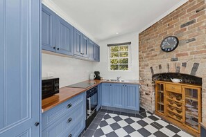 A kitchen with blue cabinets, a black and white checkered floor, a brick wall, and a clock. - 2BR Miners' Cottage, Bendigo (Bendigo)