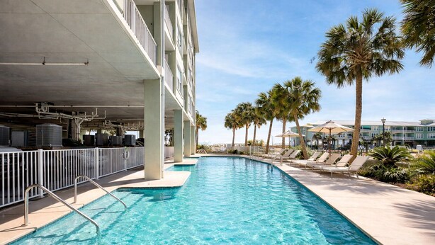 A swimming pool with a sun deck, palm trees, and a building with balconies. - Beach N Bay 2 BR Navy Cove Condo w\ FREE Boat Slip (Gulf Shores)