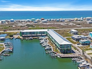 A marina with boats docked, a large building with a green roof, and a coastal view. - Beach N Bay 2 BR Navy Cove Condo w\ FREE Boat Slip (Gulf Shores)