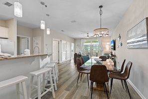 A spacious kitchen with white bar stools, a dining area with a glass table and brown chairs, and a chandelier. - Beach N Bay 2 BR Navy Cove Condo w\ FREE Boat Slip (Gulf Shores)