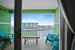 A balcony with turquoise chairs, a table, and a view of a building across the water. - Beach N Bay 2 BR Navy Cove Condo w\ FREE Boat Slip (Gulf Shores)