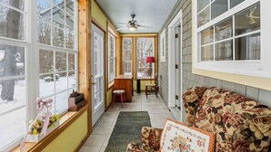A sunroom with large windows, a ceiling fan, a wooden bench, and a floral sofa. - Storybook Craftsman Cottage - Annapolis Valley (Aylesford)