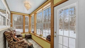 A sunroom with large windows, a chandelier, and a wooden bench. - Storybook Craftsman Cottage - Annapolis Valley (Aylesford)