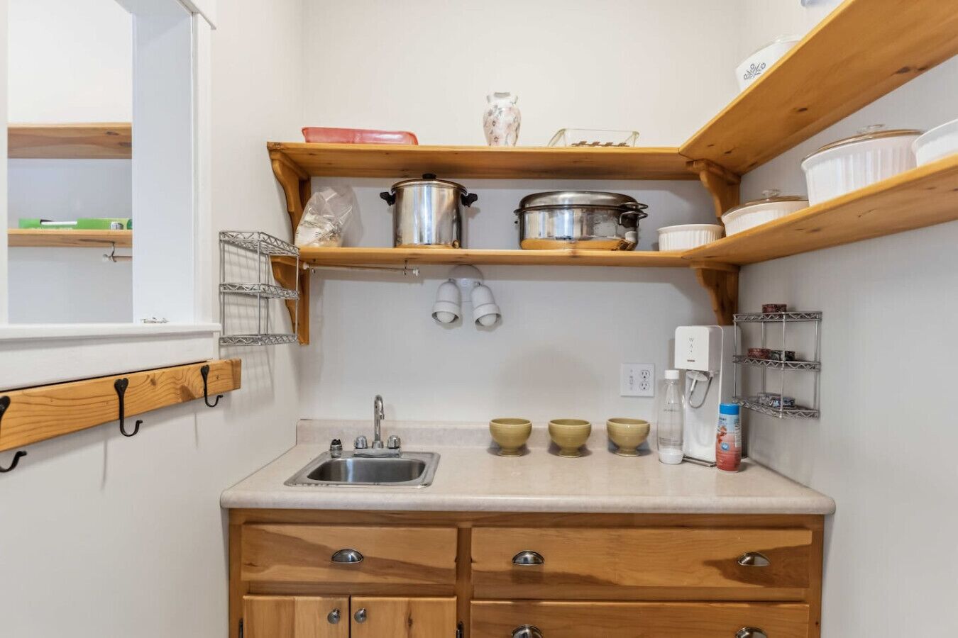 Une petite cuisine équipée d’un évier, de meubles en bois et d’étagères où sont rangées des casseroles et des bols.
