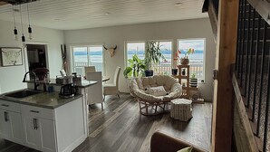 Un vaste espace de vie comprenant une cuisine, une table à manger, un fauteuil confortable et une vue sur l’extérieur.