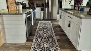 Une cuisine moderne avec des meubles blancs, des appareils en acier inoxydable, un tapis à motifs et des luminaires suspendus.