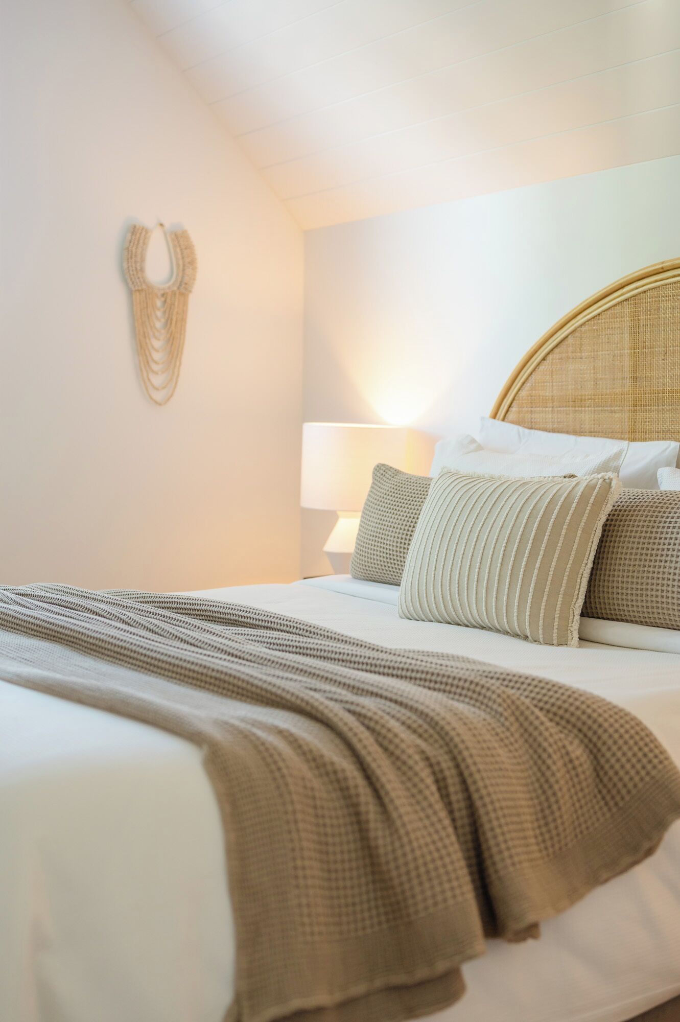 Una cama bien hecha con una colcha a rayas, un cabecero tejido y un adorno de macramé en la pared.
