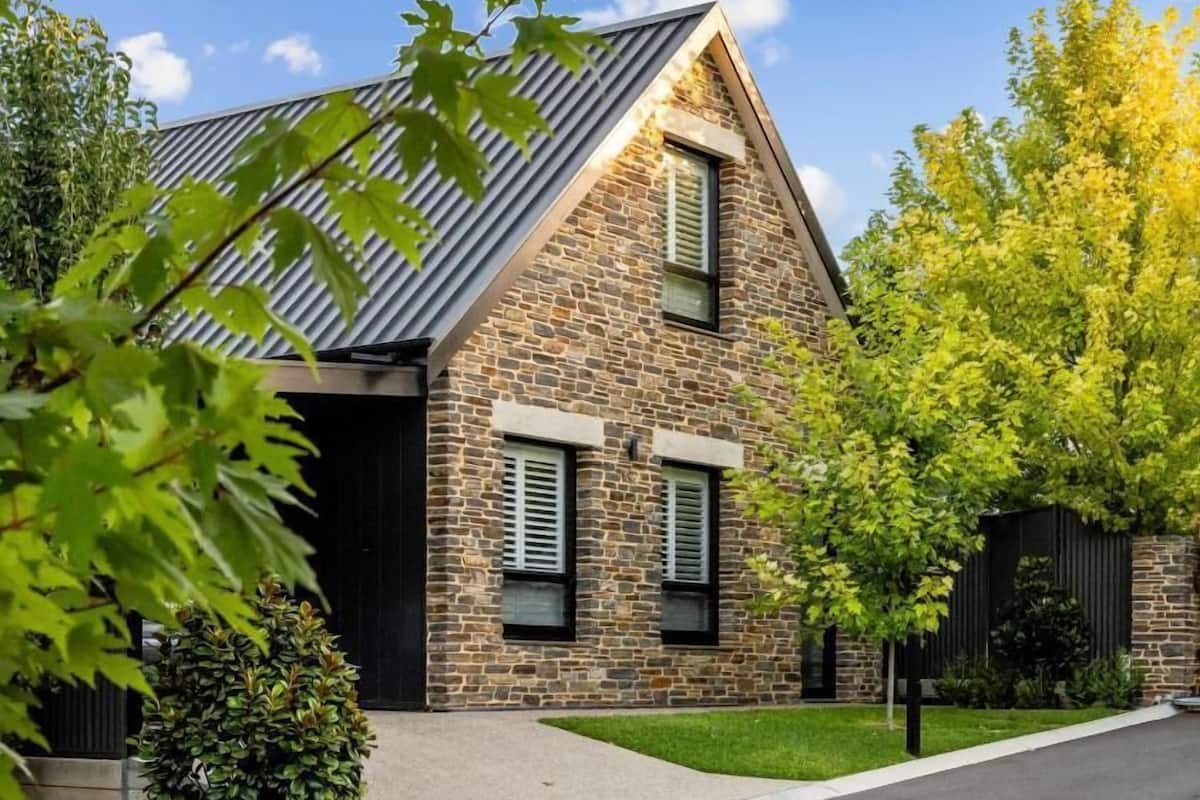 A stone house with a sloped roof, two windows with shutters, and a well-maintained lawn.