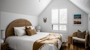 A bedroom with a bed, a ceiling fan, a window with blinds, a wall-mounted light, and a picture on the wall.