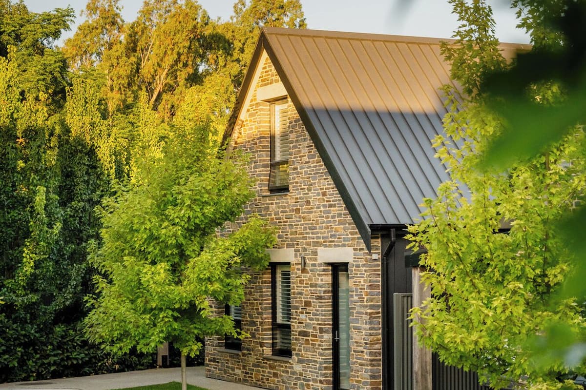 A modern house with a stone facade, a metal roof, and a well-maintained lawn.