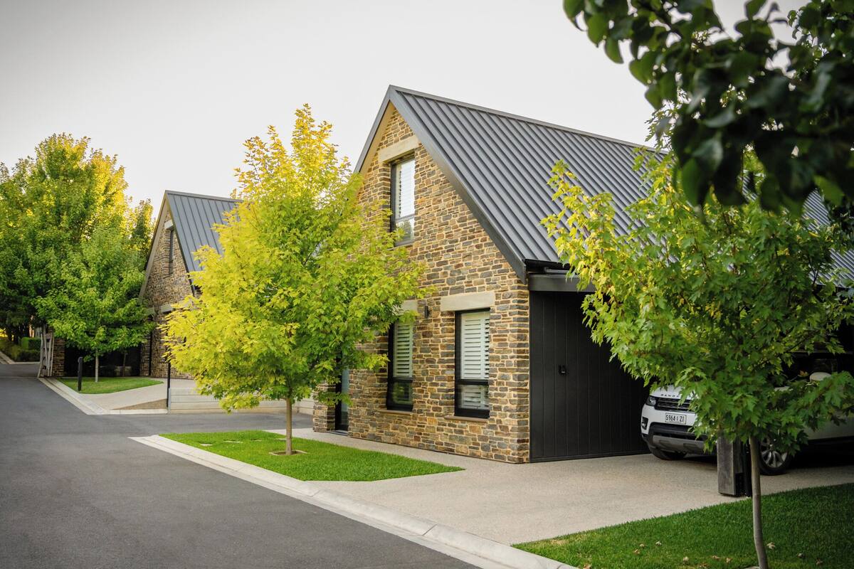 A row of modern houses with stone facades and metal roofs, surrounded by well-maintained lawns and trees.