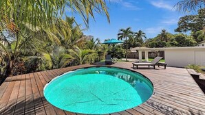 A wooden deck with a swimming pool, palm trees, and a lounge area with chairs and umbrellas. - 3-bedroom house in lovely Fort Lauderdale with AC (Fort Lauderdale)