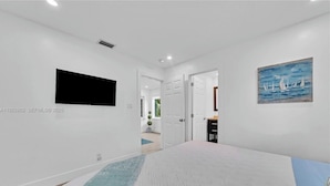 A bedroom with a bed, a flat-screen TV mounted on the wall, and a painting of sailboats. - 3-bedroom house in lovely Fort Lauderdale with AC (Fort Lauderdale)
