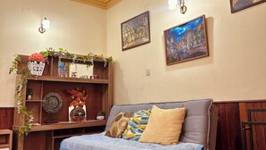 Una sala de estar con sofá, estantería de madera, obra de arte colgada en la pared y lámpara del techo.