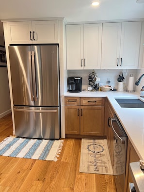 A kitchen with stainless steel appliances, wooden cabinets, a coffee maker, and a decorative rug. - Modern Family Home in Middletown, RI - just 4 miles from Newport! (Middletown)