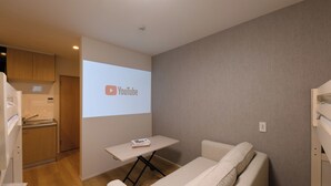 A modern room with a sofa, a small table, a kitchen area, and a projection screen displaying the YouTube logo. - TD STAY TOKYO (Tokyo)
