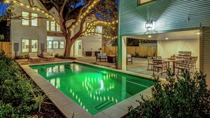 Un jardin avec une piscine, un coin repas et un grand arbre décoré de guirlandes lumineuses.