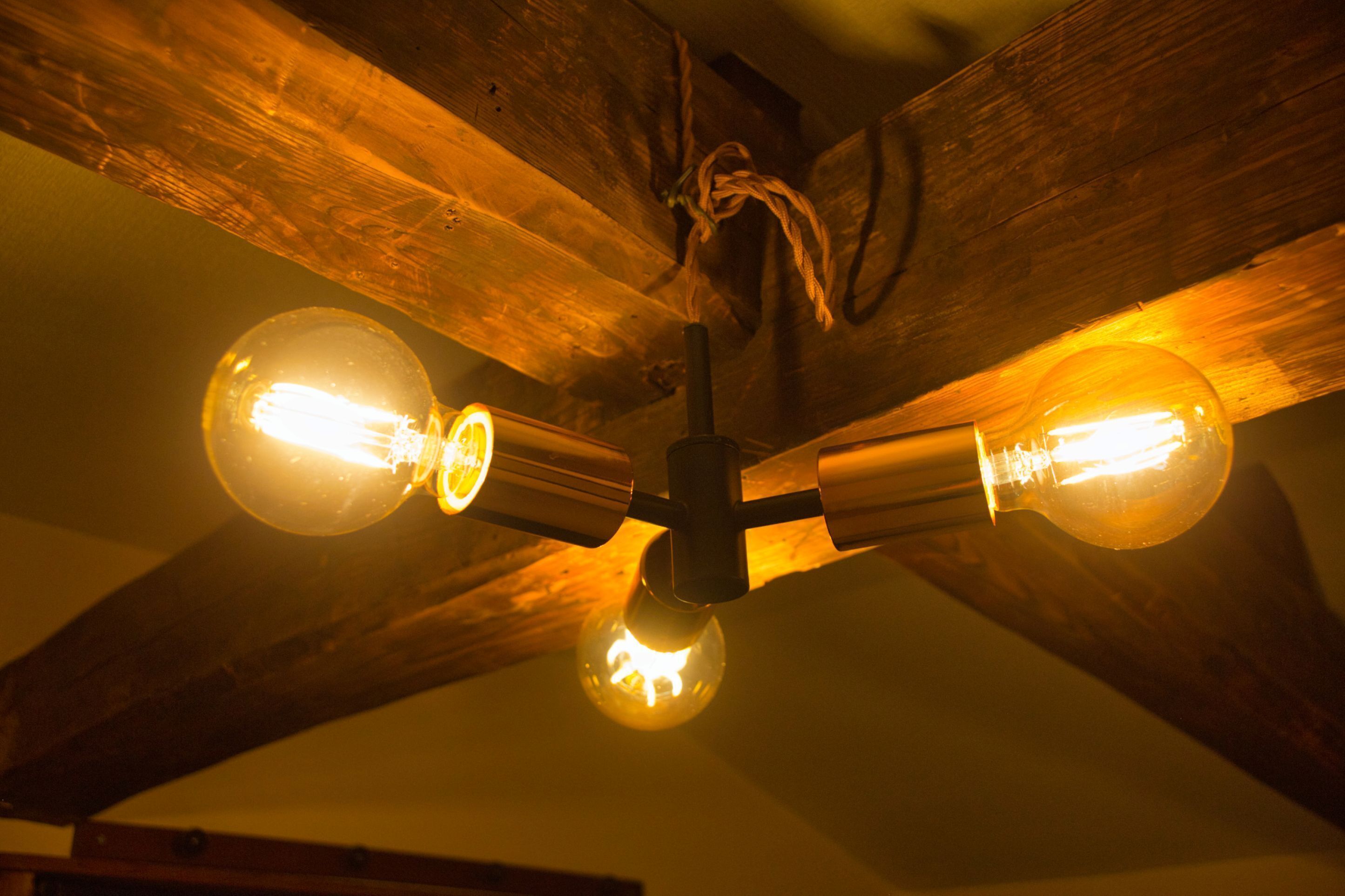 A ceiling fan with four exposed wooden beams and four exposed light bulbs.