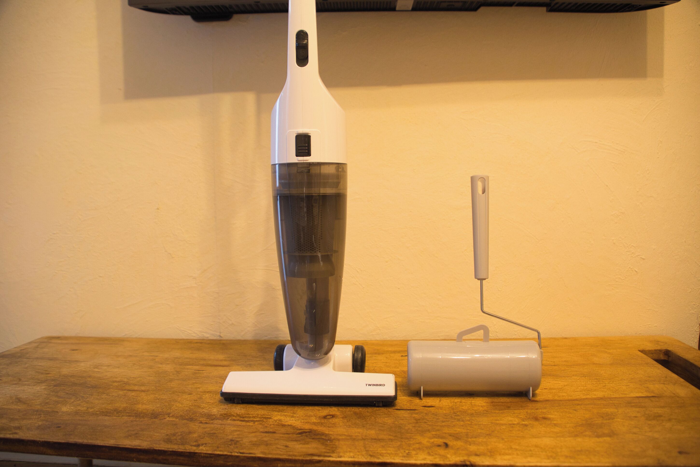 Una aspiradora blanca y una herramienta eléctrica sobre una mesa de madera.