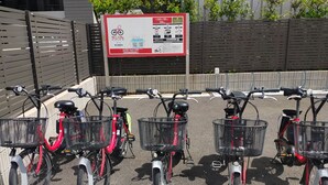 Varias bicicletas estáticas con cestas, un cartelón al fondo y una barrera metálica.