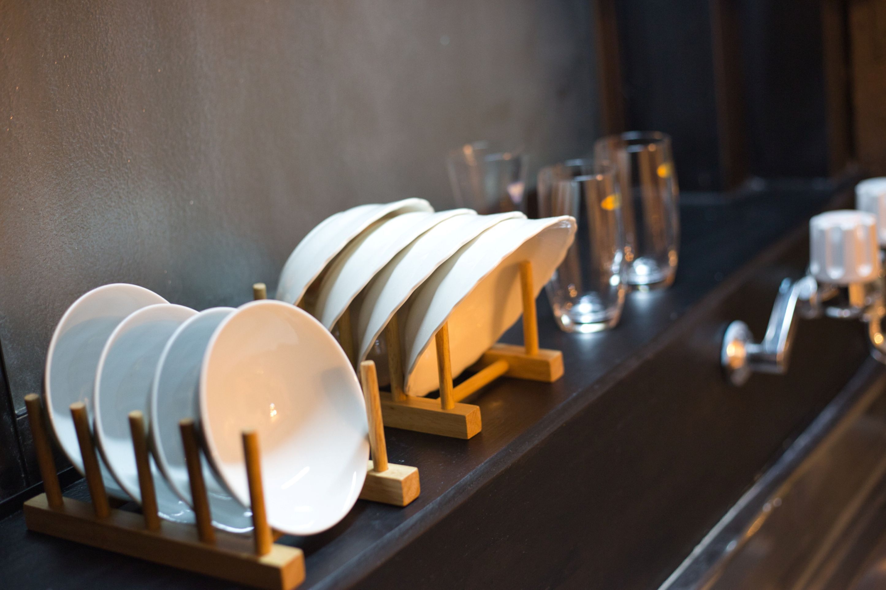 Un ensemble d’assiettes et de bols blancs, posés sur des supports en bois, disposés sur un plan de travail foncé.