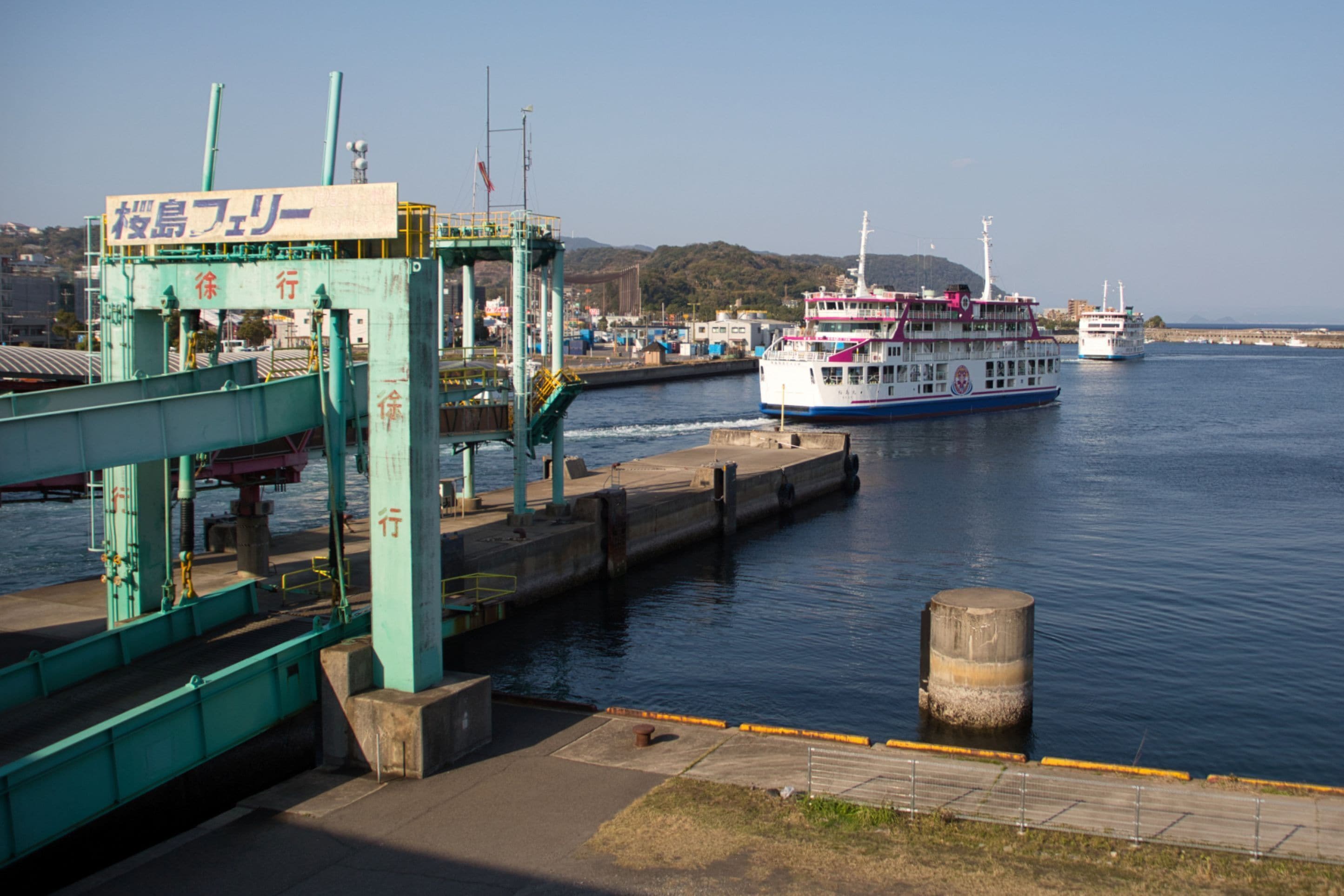 A ferry dock with a large ferry and a smaller boat in the water.