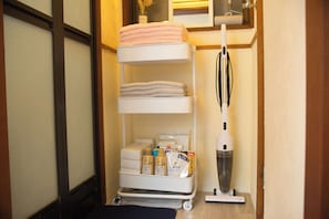 A storage cart with towels, toiletries, and a vacuum cleaner in a hotel room.