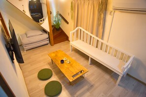 A small, cozy room with a wooden table, two green stools, a white bench, a TV, and a staircase leading to another area. - MINKAGO Kagoshima ekimae1 KG1 (Kagoshima city Ogawa cho)