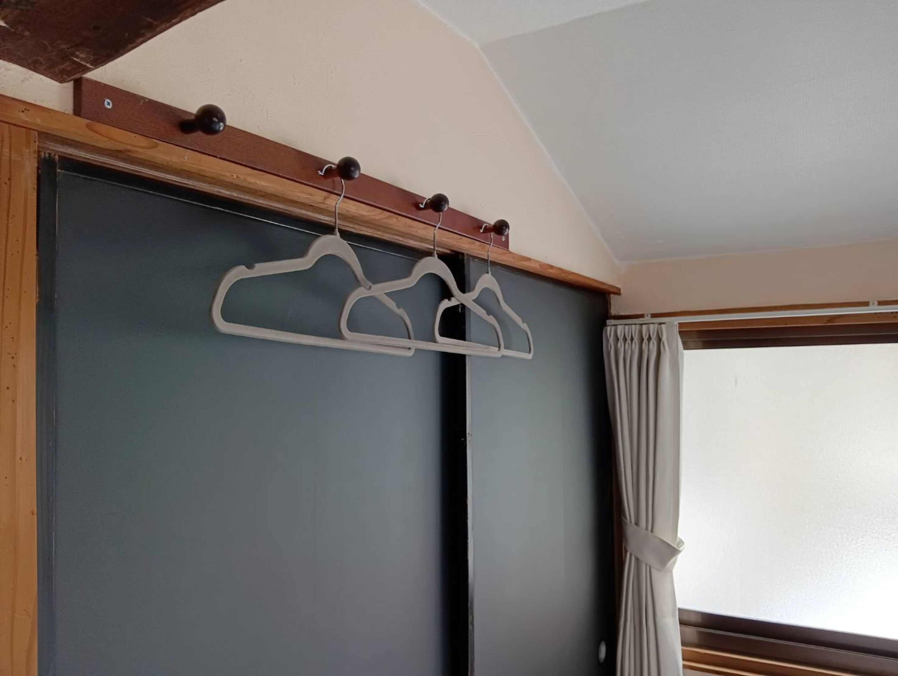 Una habitación con techo de madera, una puerta gris y una ventana con cortinas.