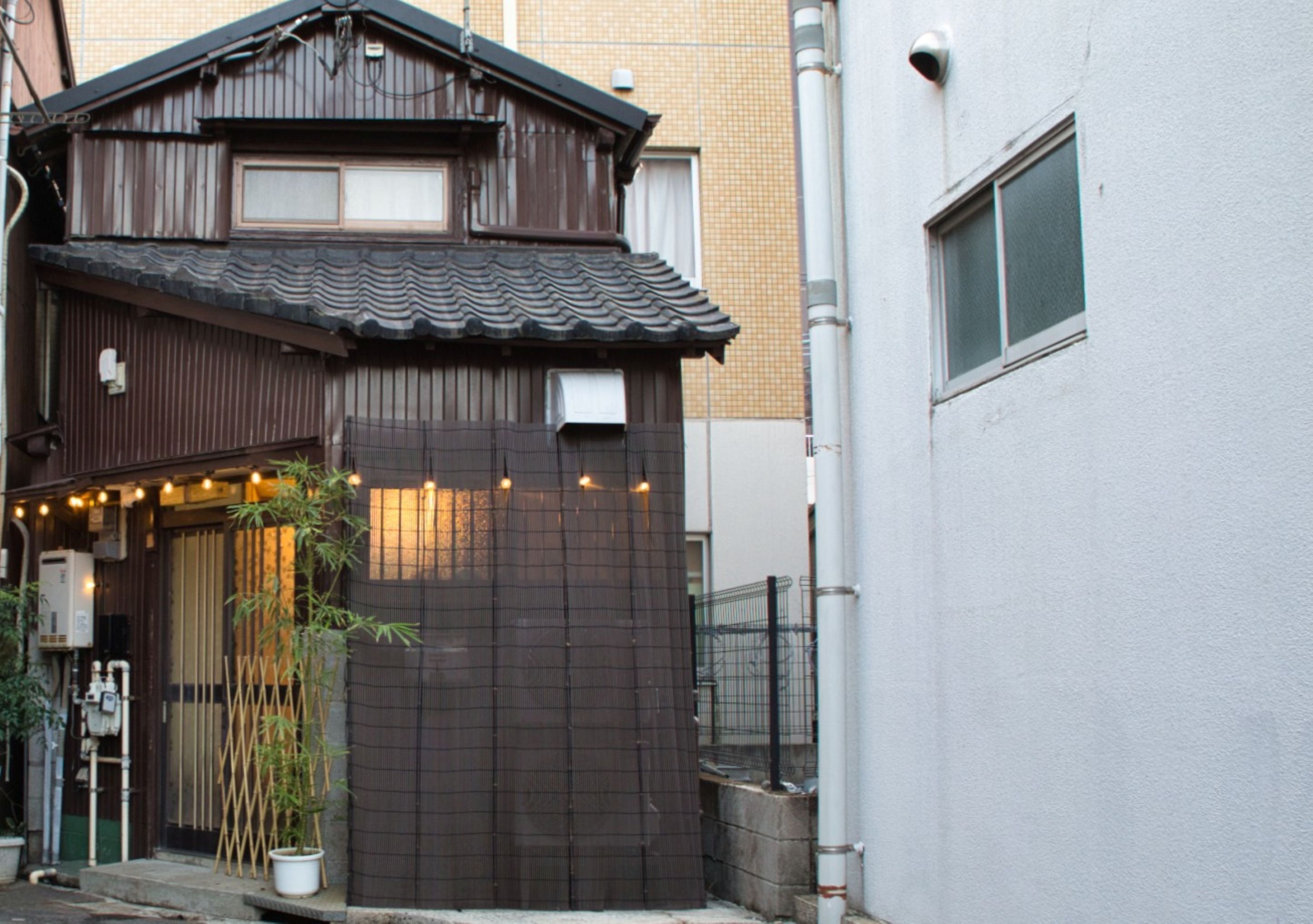 Perinteinen japanilainen rakennus, jossa on tiilikatto, puinen portti ja ruukussa oleva bambukasvi.