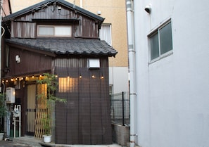 A traditional Japanese building with a tiled roof, a wooden gate, and a potted bamboo plant.