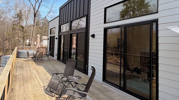 A modern house with a deck, large windows, and outdoor furniture. - Brand new riverfront home with private beach, modern, serene, central HV spot. (High Falls)