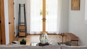 A living room with a sofa, a ladder, a table, and a large window. - Brand new riverfront home with private beach, modern, serene, central HV spot. (High Falls)