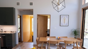 A modern kitchen with dark cabinets, a dining area with a wooden table and chairs, and a bright yellow cushion on a grey sofa. - Brand new riverfront home with private beach, modern, serene, central HV spot. (High Falls)