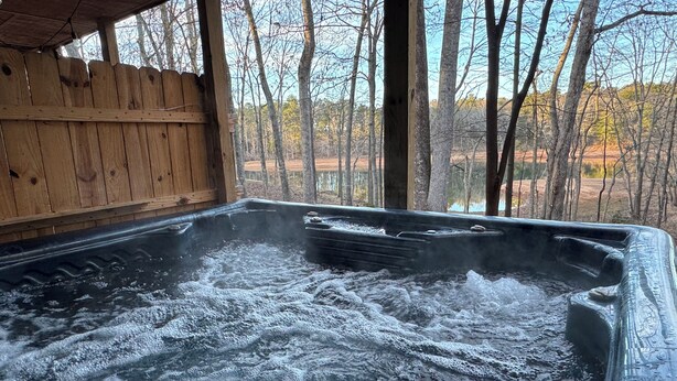 Un jacuzzi con muelle de madera y vista a árboles y un lago.