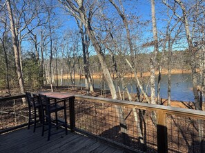 Eine Holzterrasse mit Stühlen und einem Tisch mit Blick auf einen von Bäumen gesäumten See.