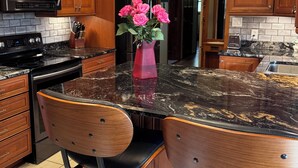 Una cocina con armarios de madera, encimera negra, electrodomésticos de acero inoxidable y un florero con flores rosas.
