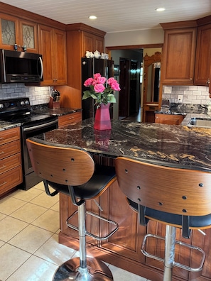 Una cocina con armarios de madera, encimera negra, electrodomésticos de acero inoxidable y un florero con flores rosas.