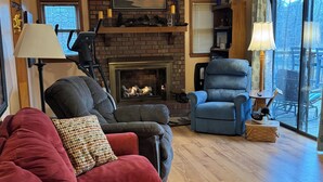Un salón con chimenea, un sofá rojo, un sillón azul y vistas a través de amplios ventanales.