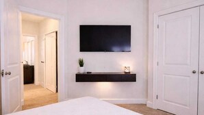 A bedroom with a large bed, a mounted TV, a bedside table with a plant, and a door to another room. - Lux in Black 2BR Bay, Pool & Ocean Views (Fort Myers)