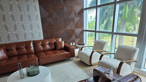 A modern living room with a brown leather sofa, a white round coffee table, and a beige armchair. - Lux in Black 2BR Bay, Pool & Ocean Views (Fort Myers)