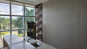 A modern bathroom with a large window, a marble sink, and a wall-mounted gaming console. - Lux in Black 2BR Bay, Pool & Ocean Views (Fort Myers)