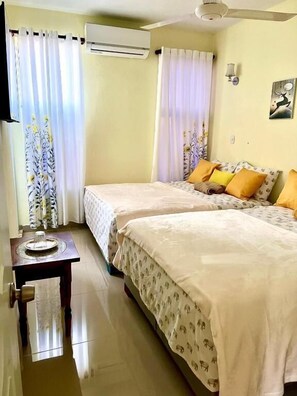 A hotel room with two beds, a flat-screen TV, an air conditioner, and a small table with a tray. - Hotel Maria Bonita Higüey (Higuey)