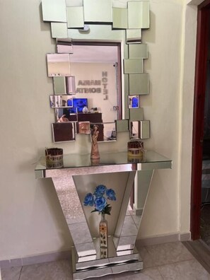 A modern interior with a glass console table, a decorative vase with blue flowers, and a mirror with multiple smaller mirrors. - Hotel Maria Bonita Higüey (Higuey)