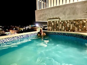 A swimming pool with a stone wall and a view of a cityscape at night. - Hotel Maria Bonita Higüey (Higuey)