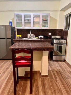 A compact kitchen with granite countertops, a built-in stove, and a refrigerator. - Hotel Maria Bonita Higüey (Higuey)
