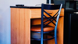 Une chambre d’hôtel compacte comprenant un bureau en bois, une chaise noire, un miroir rond, une lampe et un four à micro-ondes.