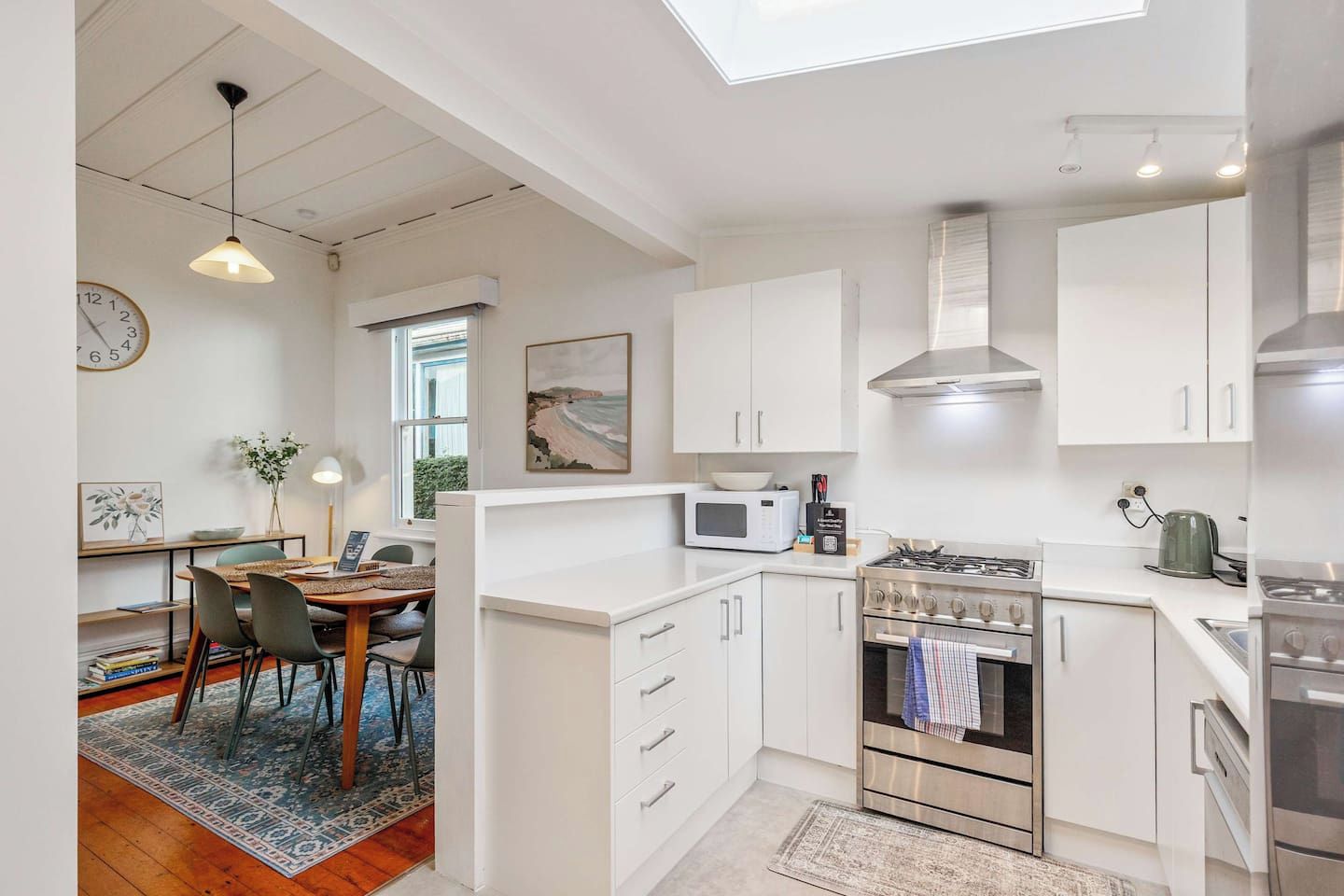 A modern kitchen with white cabinetry, a gas stove, a microwave, and a dining area with a table and chairs.