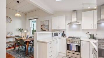 A modern kitchen with white cabinetry, a gas stove, a microwave, and a dining area with a table and chairs.